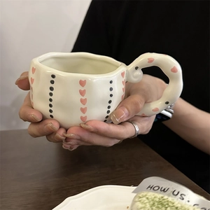 Handheld shot of a cream ceramic coffee mug with pink hearts and a spiral handle