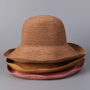 Detail of stacked handmade raffia sun hats in brown and pink with wide wavy brims