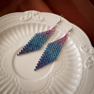 Détails de boucles d'oreilles géométriques à pompons et strass dégradés sur une assiette blanche
