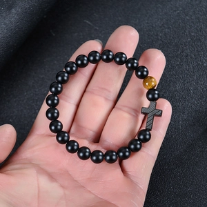 Matte black onyx bracelet with tiger eye stone and cross charm on a textured background