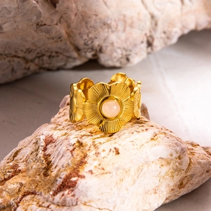 Gros plan sur la bague fleur dorée avec pierre rose sur fond de pierre naturelle