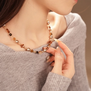 Close-up of geometric tiger eye and pearl beaded necklace on a model for autumn style