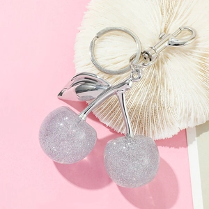Detail of transparent cherry keychain with silver glitter and metallic leaf charm