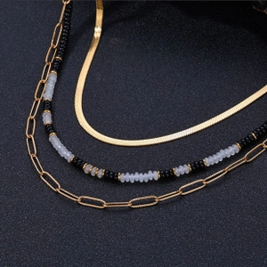 Macro shot of double-layered gold snake chain and paperclip link with black beaded necklace