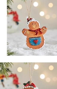 Detail of gingerbread man ornament with red hat and rope hanger on a snowy Christmas tree