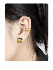 Close-up of minimalist textured gold ear cuff and black gold stud on model's ear