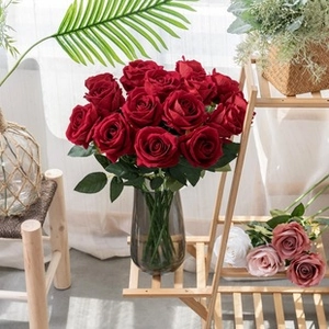 Close-up of artificial red roses in a dark grey glass vase with natural sunlight