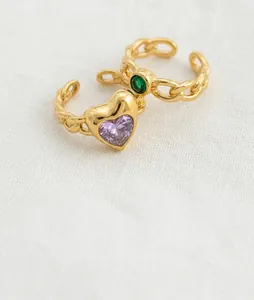 Close-up of gold chain-textured rings featuring heart-shaped purple and green gemstones