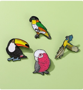Detail view of four colorful enamel bird pins featuring toucan and parrot designs