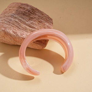 Detail of pink acrylic C-shaped open cuff bracelet with marble texture against rocks