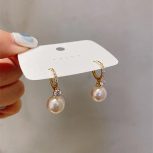 Detail of elegant gold earrings with pave-set zircons and large round light gold pearls
