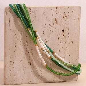 Detail of multi-layered beaded necklace with green crystals and white pearls on stone