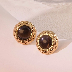 Close-up of vintage round gold-rimmed stud earring with dark brown gem and lattice texture