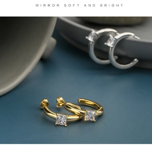 Close-up of C-shaped gold earrings with princess-cut cubic zirconia in mirror finish