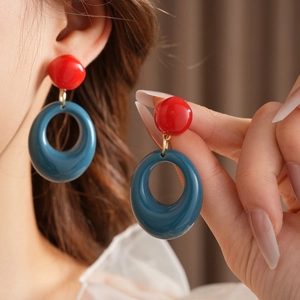Macro shot of geometric resin drop earrings in bold red and blue with gold accents