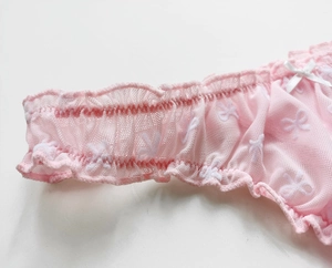 Detail of pink mesh lace thong with white bow pattern and elastic ruffle waistband