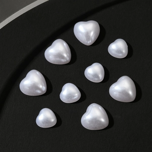 Macro shot of white heart-shaped faux pearl beads with soft luster on dark texture