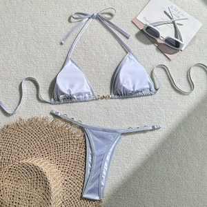 Detailed flat lay of a shimmering silver bikini with chic gold rings and summer accessories