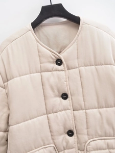 Detail of beige quilted jacket featuring round neck, black buttons, and twill fabric texture