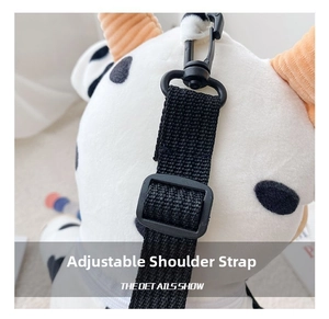 Detail view of the plush cow bag featuring an adjustable black nylon shoulder strap