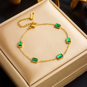 Detail of gold chain bracelet with emerald green stones on champagne jewelry box
