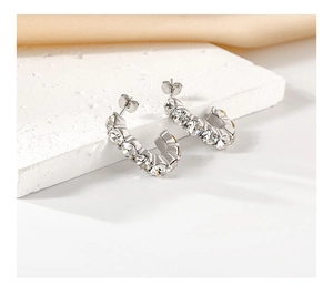 Detailed close-up of silver C-shaped crystal earrings on stone and silk background