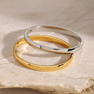 Polished stainless steel gold and silver cuff bracelets displayed on a natural rock surface