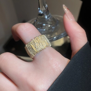 Close-up of a wide gold textured metal ring featuring a woven design on a hand