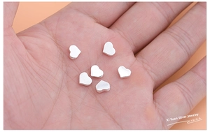 Close-up of six small S925 sterling silver heart beads for DIY jewelry making in a hand