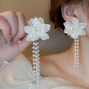Detailed view of white flower earrings with long pearl tassels worn by a model