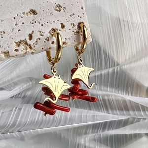 Macro detail of gold manta ray earrings with vibrant red coral-inspired accents