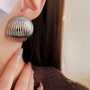 Close-up of minimalist silver striped round stud earrings worn by a model in soft light
