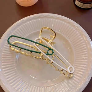 Detail of elegant gold safety-pin hair clip with green and white lacquer on ceramic tray
