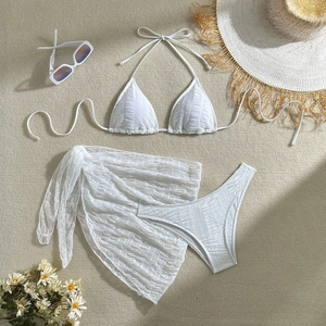 Flat lay of white three-piece bikini set with ribbed texture and sheer mesh sarong