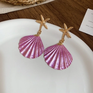 Detailed close-up of golden starfish stud earrings with purple seashell pendants on ceramic