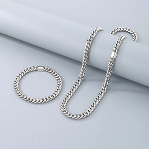 Polished stainless steel Cuban link chain necklace and bracelet set on grey display pedestal