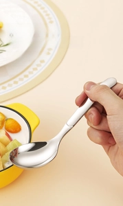 Polished stainless steel round spoon held by hand over a yellow ceramic bowl in kitchen