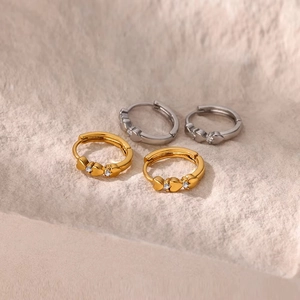 Macro shot of gold and silver heart huggie earrings with cubic zirconia on stone surface