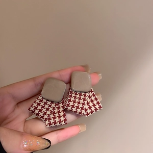 Close-up of red and white houndstooth fabric earrings with beige square studs