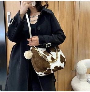 Detailed close-up of plush cow print tote bag with gold chain strap and fluffy pompom