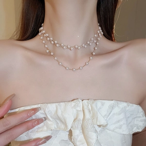 Détail d'un collier double rang en perles artificielles et chaîne dorée porté par un mannequin