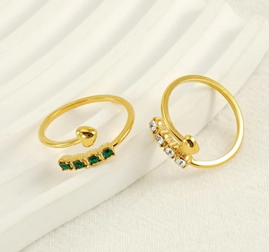 Detail of adjustable gold rings featuring green and white zircons with a heart motif