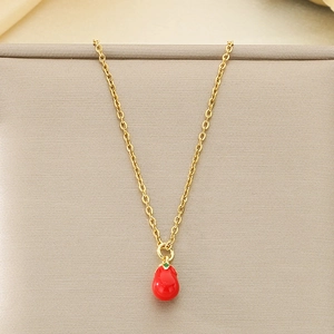 Dettaglio di una collana dorata con pendente a peperone rosso in smalto su base in tessuto