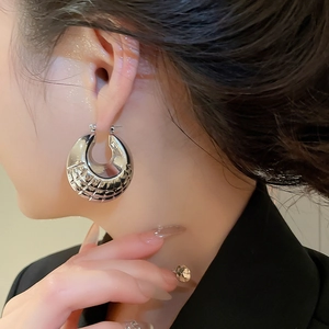 Macro detail of large silver hoop earring with embossed geometric pattern on female model
