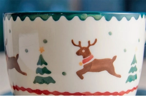 Detailed close-up of hand-painted Christmas ceramic mug with elk and tree patterns