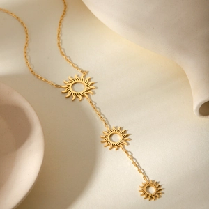 Detailed view of gold Y-shaped necklace with three hollow sun pendants on a warm background