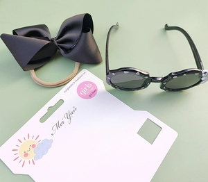 Detail of girls' black polka dot sunglasses and bow headband set on card packaging