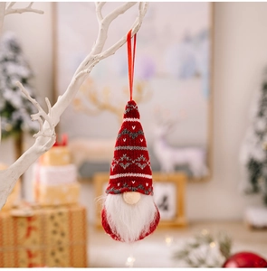 Detail of red knitted Christmas gnome ornament with white beard hanging on a branch