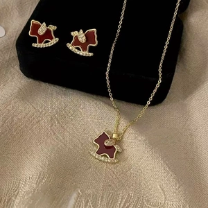 18K gold plated horse jewelry set with red enamel and crystals on beige fabric