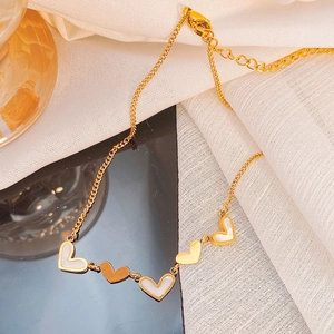 Detail of 18K gold plated necklace with five white shell heart charms on a sleek surface